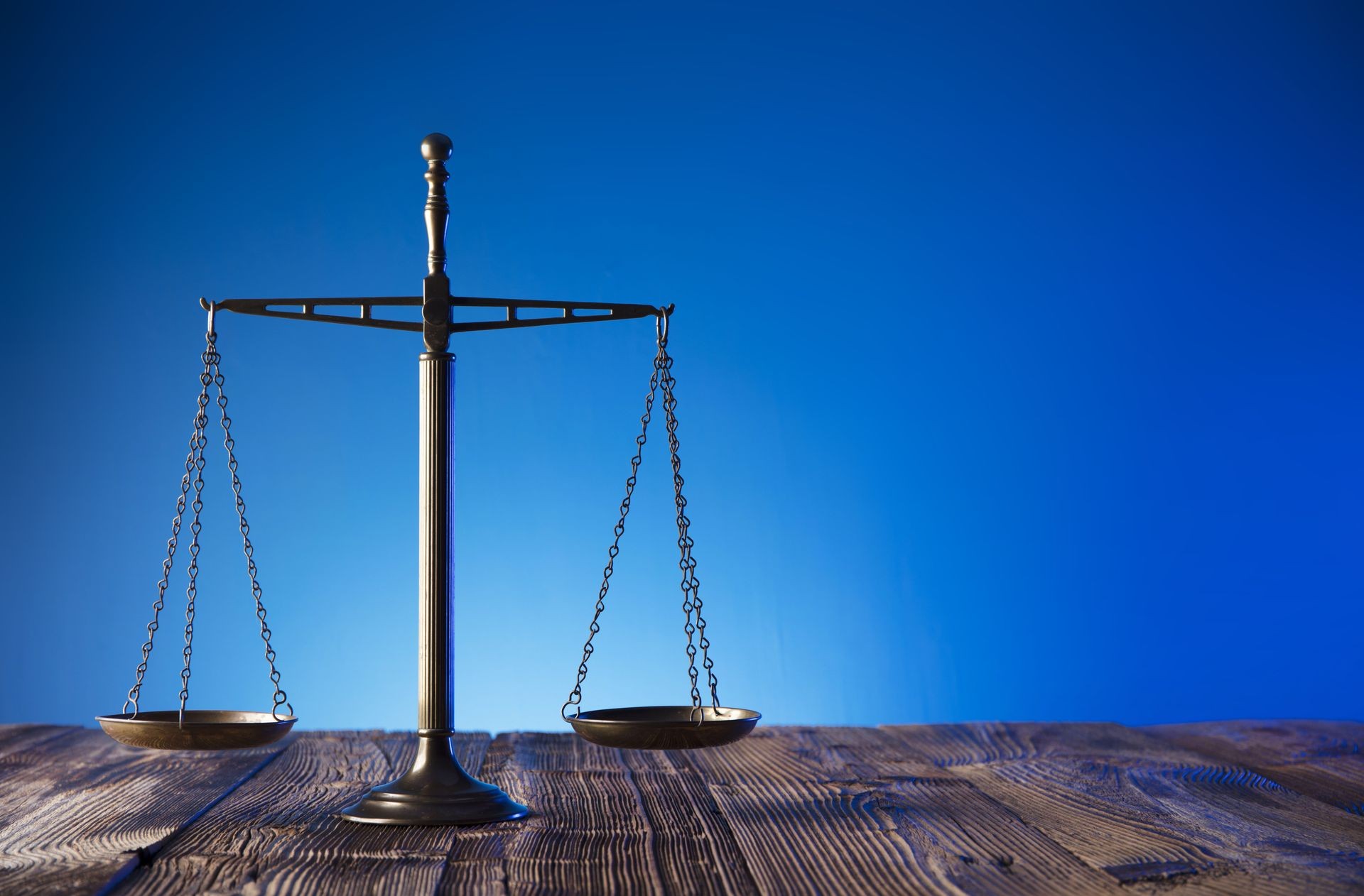 Scales of justice on old wooden table and blue background. Law theme and concept.